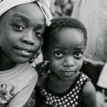 Black and white glad children in casual clothes standing on authentic town street and looking at camera with curiosity